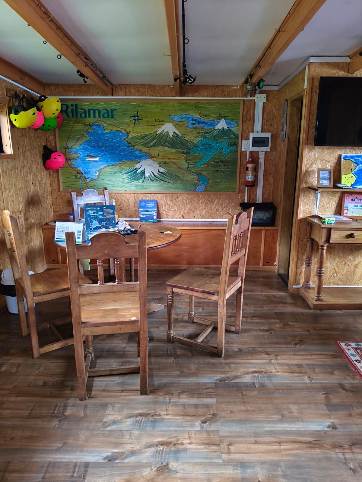 Interior de la oficina con un gran mapa pintado del Lago Llanquihue y sus volcanes, mesa y sillas de madera