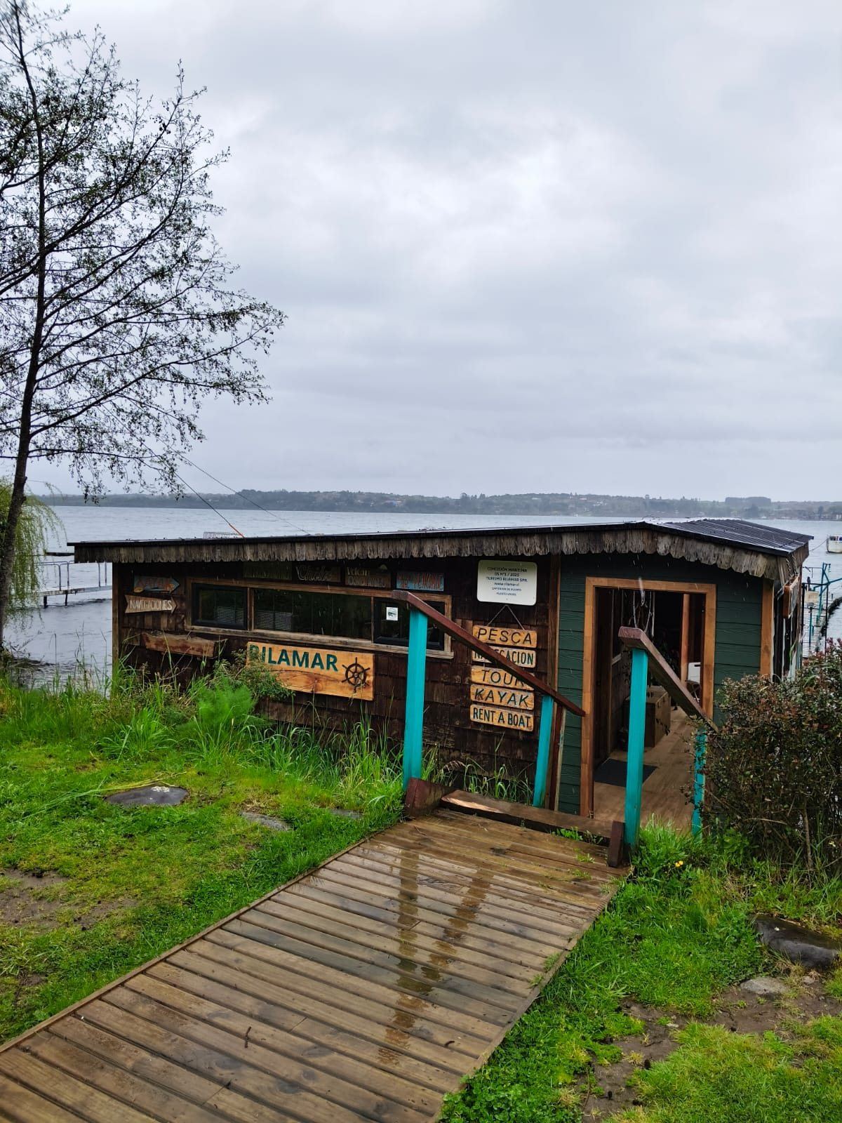 Pasarela de madera hacia la oficina Rilamar, con letreros de pesca, navegación, tour, kayak y arriendo de botes, junto al lago